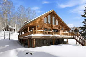 Back of property featuring log siding, stone siding, and a deck