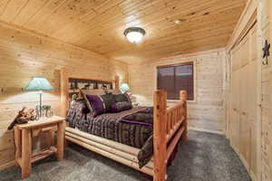 Bedroom with wood walls, dark colored carpet, a closet, and wooden ceiling