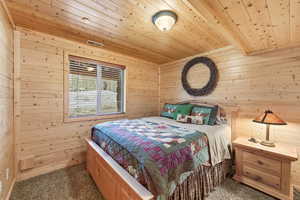 Bedroom featuring wood walls, dark carpet, and wooden ceiling