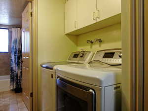 Laundry area with light tile patterned floors, separate washer and dryer, cabinet space, and a textured ceiling