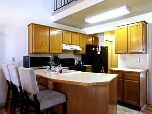 Kitchen featuring light countertops, a peninsula, a breakfast bar, wood finish cabinetry, and vaulted ceiling
