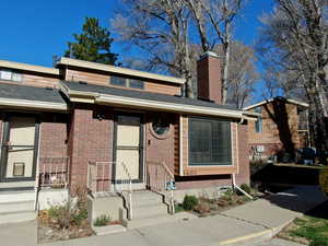 View of front facade featuring brick siding, a chimney, and roof with shingles