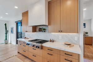 Kitchen with recessed lighting, light wood finished floors, decorative backsplash, light stone countertops, and stainless steel gas stovetop
