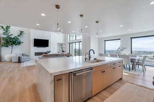Kitchen with an island with sink, light stone counters, light wood-type flooring, and stainless steel dishwasher