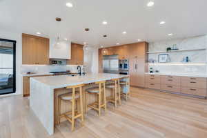 Kitchen with open shelves, light stone counters, decorative backsplash, a large island, and light wood finished floors