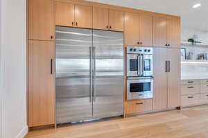 Kitchen with stainless steel appliances, light wood finish cabinets, light wood-style floors, open shelves, and recessed lighting