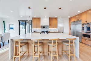 Kitchen featuring light stone countertops, a large island, stainless steel appliances, and light wood finish cabinets