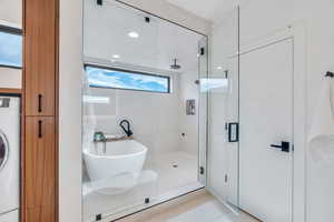 Bathroom with washer / dryer, a stall shower, a freestanding tub, recessed lighting, and light tile patterned floors