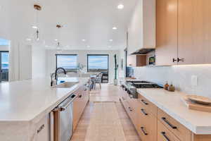 Kitchen featuring light stone countertops, tasteful backsplash, stainless steel appliances, light wood-style floors, and hanging light fixtures