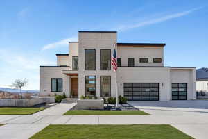 Modern home with concrete driveway, a front lawn, stucco siding, and an attached garage