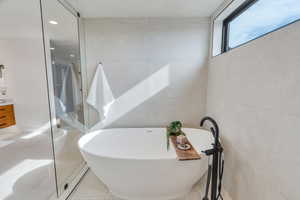 Bathroom with a shower stall, a soaking tub, vanity, tile walls, and light tile patterned floors