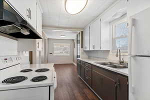 Kitchen with white appliances, two tone cabinetry, light countertops, healthy amount of natural light, and dark wood finished floors