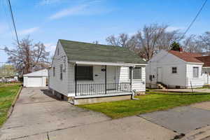 Bungalow-style house featuring an outdoor structure, a garage, covered porch, a front yard, and roof with shingles