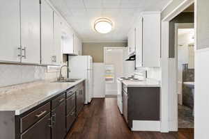 Kitchen featuring light countertops, white appliances, dark wood finished floors, dual tone cabinets, and a wainscoted wall