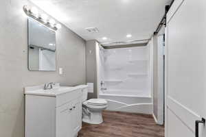 Full bath featuring vanity, a textured ceiling, dark wood finished floors, shower / bath combination, and a textured wall