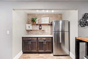 Theater/recreation room dry bar featuring dark wood finish cabinetry, freestanding refrigerator, open shelves, and light wood finished floors