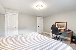 Bedroom with light colored carpet, a desk, and a textured ceiling