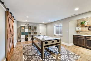 Recreation room featuring a barn door, light wood-style flooring, and recessed lighting