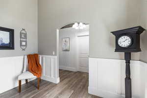 Music room with a wainscoted wall, wood finished floors, a decorative wall, suspended lighting, and arched walkways