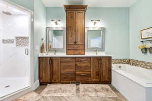 Master bath featuring double vanity, a stall shower, a bath, and light wood finished floors