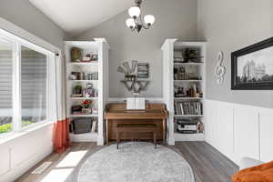 Music room with a wainscoted wall, a decorative wall, dark wood-style flooring, hanging lights, and vaulted ceiling