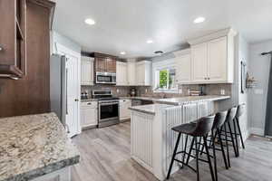 Kitchen with stainless steel appliances, a peninsula, light wood-style floors, a breakfast bar area, and light stone countertops