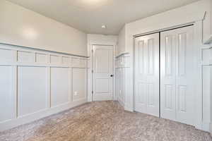 Unfurnished office/bedroom featuring a decorative wall, wainscoting, a closet, light carpet, and a textured ceiling
