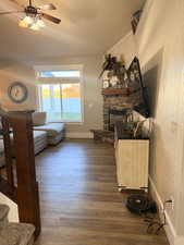 Living room with dark wood-style floors, ceiling fan, wallpapered walls, and a stone fireplace