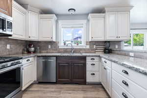 Kitchen featuring stainless steel appliances, light wood-style flooring, tasteful backsplash, light stone counters, and dual tone cabinetry