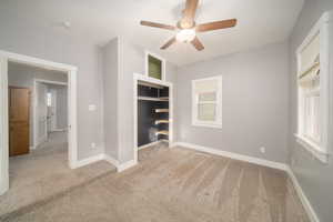 Unfurnished bedroom with light colored carpet, multiple windows, ceiling fan, and a closet