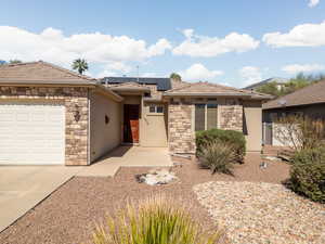 View of front of house with stone siding, solar panels, an attached garage, and stucco siding
