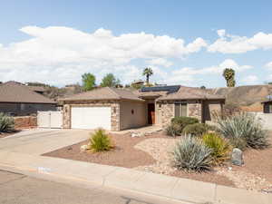 Ranch-style home with an attached garage, roof mounted solar panels, stone siding, and concrete driveway