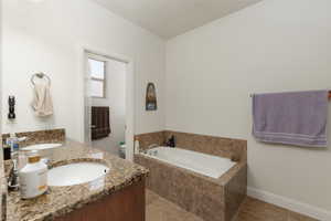Full bath with double vanity, a bath, and light tile patterned floors