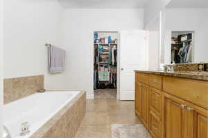 Bathroom with a spacious closet, vanity, a garden tub, and light tile patterned floors