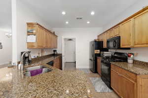 Kitchen with black appliances, dark stone countertops, light tile patterned floors, wood finish cabinets, and a peninsula
