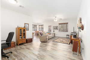 Living room with light wood finished floors, a desk, and a ceiling fan