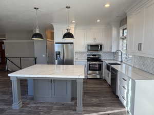 Kitchen featuring stainless steel appliances, tasteful backsplash, dark wood-style flooring, decorative light fixtures, and two tone custom cabinets