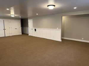 Finished below grade area with wainscoting, dark colored carpet, a decorative wall, recessed lighting, and a textured ceiling. The kids will enjoy their little kid nook behind the door and the little window.