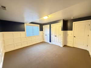 Unfurnished 4/5 bedroom with wainscoting, two closets, a decorative wall, and dark colored carpet