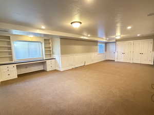 Basement with built in desk, carpet floors, a wainscoted wall, a textured ceiling, recessed lighting, double storage closets
