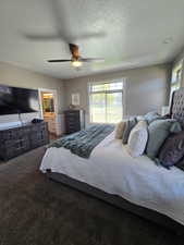 Bedroom featuring a textured ceiling, dark colored carpet, connected bathroom, and a ceiling fan