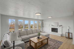 Living room featuring a textured ceiling, light wood-style floors, and a glass covered fireplace