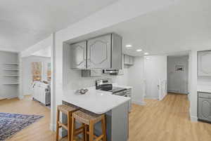 Kitchen with gray cabinets, stainless steel range with electric cooktop, a breakfast bar area, light wood finished floors, and recessed lighting