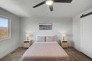Bedroom with a barn door, dark colored carpet, a textured ceiling, and a ceiling fan