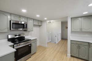 Kitchen with stainless steel appliances, recessed lighting, light wood finished floors, a textured ceiling, and light stone countertops