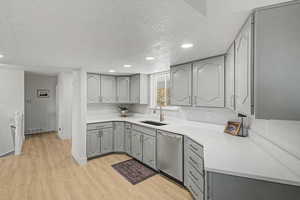 Kitchen featuring gray cabinets, a textured ceiling, dishwasher, light wood finished floors, and recessed lighting