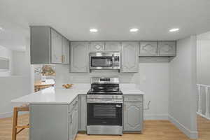Kitchen with stainless steel appliances, gray cabinets, light wood-style floors, recessed lighting, and a kitchen bar