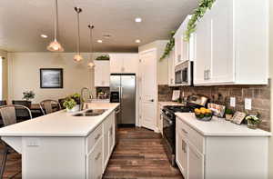 Kitchen featuring a breakfast bar, stainless steel appliances, a kitchen island with sink, white cabinetry, and decorative light fixtures
