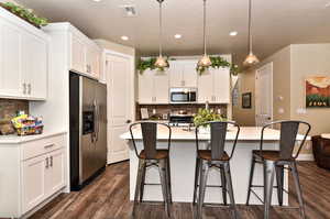 Kitchen featuring a center island with sink, a kitchen bar, stainless steel appliances, and white cabinetry