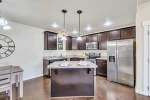 Kitchen featuring dark wood finish cabinetry, stainless steel appliances, a center island, light stone countertops, and dark wood finished floors